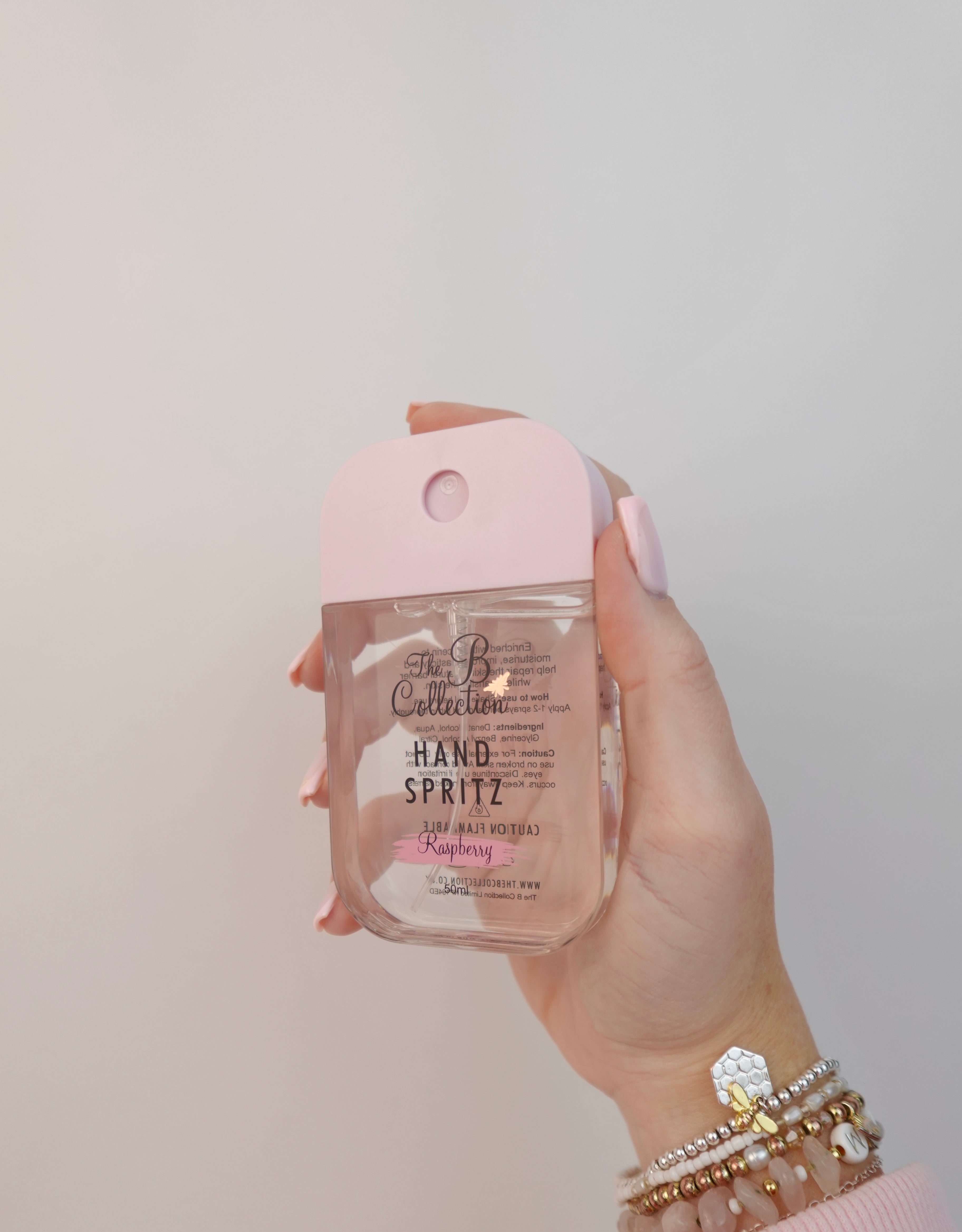 Hand holding a bottle of hand sanitizer with a pink cover against a plain background