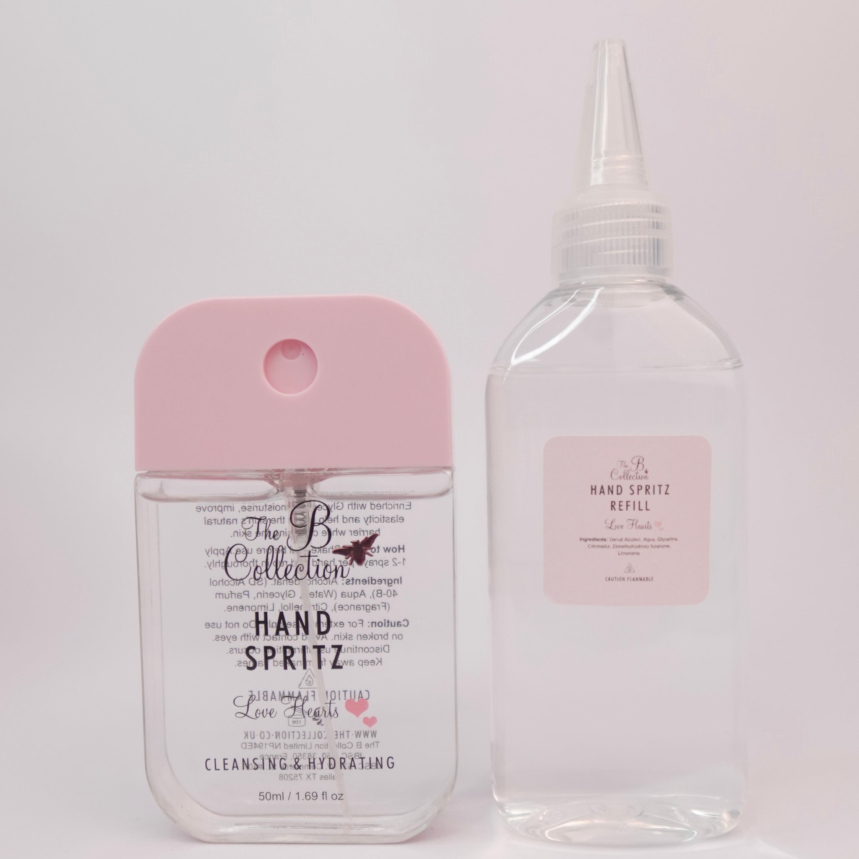 A hand spray bottle with a light pink cap next to a clear refill bottle with a pointed white cap, both labeled 'The B Collection' on a plain light background.